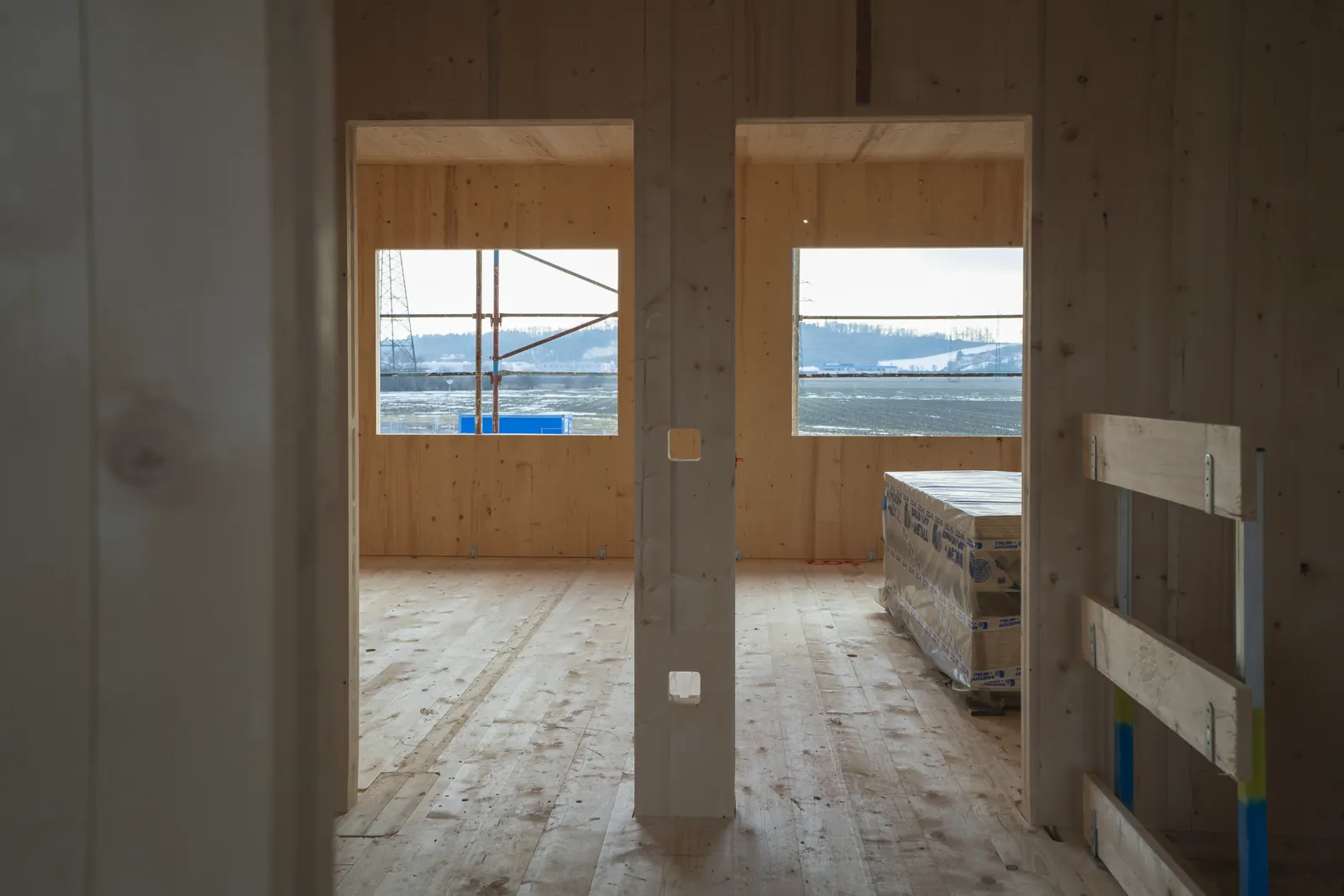 Blick durch zwei Türöffnungen im Massivholz-Rohbau: die Wandflächen sind sichtbares Holz, in der Wand sind die Aussparungen für die Steckdosen bereits ausgefräst, dahinter die Fensteröffnungen