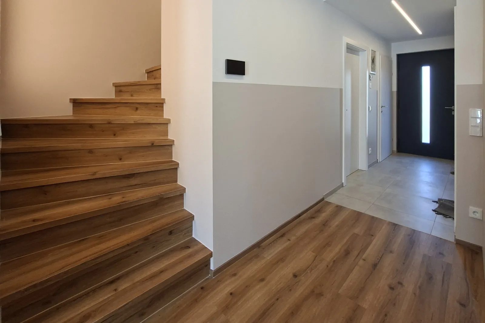 Blick vom Wohnraum über die gewendelte Holztreppe und den Flur zur Haustür der Doppelhaushälfte in Asten